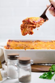 a person is taking a piece of lasagna out of the casserole dish