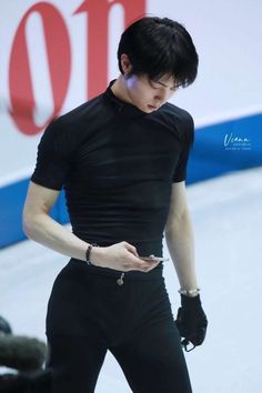 a man in black is looking at his cell phone while standing on an ice rink