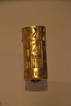 a gold ring with an egyptian design on the front and side, hanging from a wall