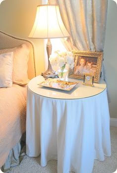 a small table with a lamp and pictures on it next to a bed in a bedroom