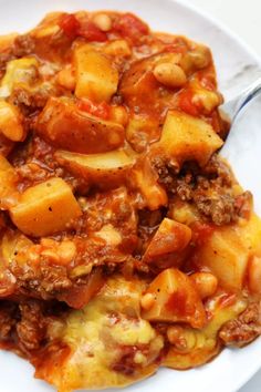 a white plate topped with pasta and meat covered in sauce on top of a table