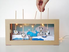 a hand is holding an open box with candles in it and penguins on the inside