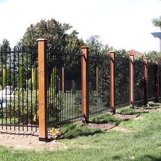 an iron fence with wood posts and green grass