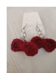 two red crocheted hearts are attached to silver metal chains on a white wooden surface