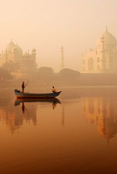 two people in a small boat on the water near a large white building with many spires