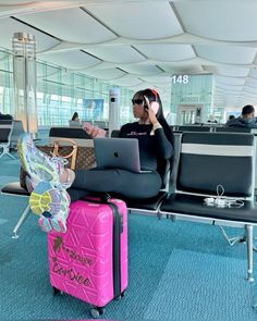 a woman sitting on top of a pink suitcase in an airport