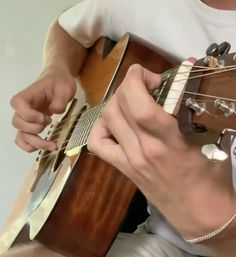 a man is playing an acoustic guitar while sitting down with his hands on the strings