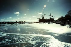 an old ship sitting on top of a sandy beach next to the ocean under a blue sky