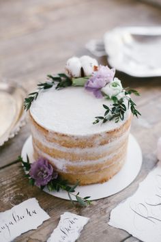 a wedding cake with flowers on top is sitting on a table next to place cards