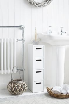 a white bathroom with a sink, towel rack and basket on the floor next to it