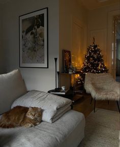 an orange cat laying on top of a white couch in front of a christmas tree