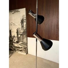 two black lamps sitting on top of a metal pole next to a wall mounted painting