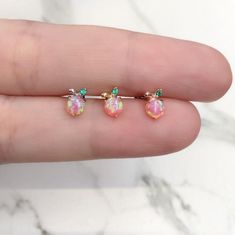 a person is holding three tiny opal studs in their hand, one with green and pink stones on it