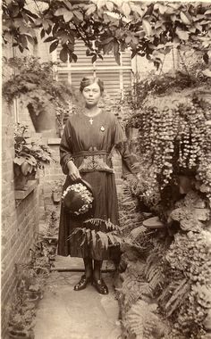 an old black and white photo of a woman standing in a garden with plants around her