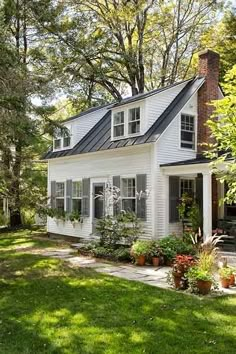 a small white house in the middle of some trees and grass with potted plants