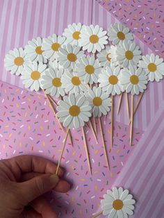 a hand is holding some daisies on sticks