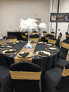 black and gold table cloths are set up for a formal function with white feathers on top