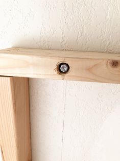 a wooden shelf with a metal knob on it's end and a white wall in the background