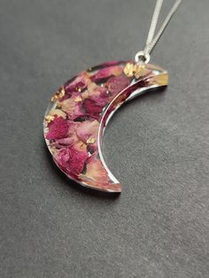 a necklace with flowers on it sitting on a gray surface and the moon is in the background