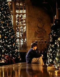 a man sitting on the floor next to a christmas tree in a room filled with lights