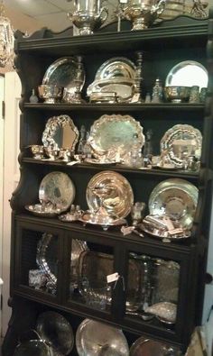 a black china cabinet with lots of silver plates on it and glass dishes in the bottom shelf