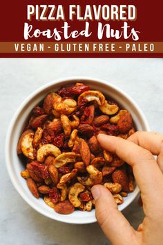 a bowl filled with roasted nuts on top of a white counter next to a hand pointing at it