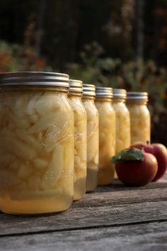 four jars filled with food sitting on top of a wooden table next to an apple