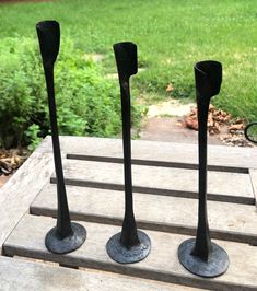 three black metal vases sitting on top of a wooden table next to a green field