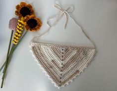 a crocheted triangle next to a flower on top of a white tablecloth