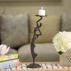 a candle holder on a table with flowers and books next to it in front of a couch