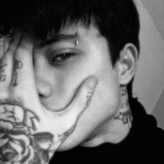 a young man with tattoos covering his face and hand over his mouth while looking at the camera