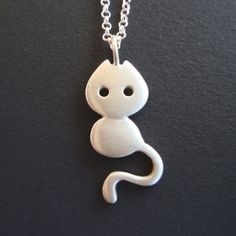 a white cat pendant is hanging on a silver plated chain with a black background