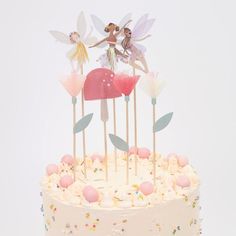 there is a cake that has three fairy wands on top of it, and two little tinkerbells on the top