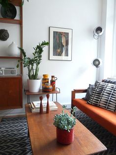 a living room filled with furniture and plants on top of a wooden table in front of a window