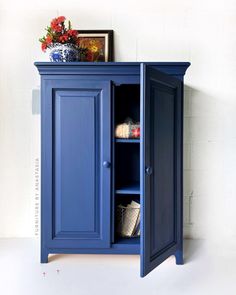 a blue cabinet with an open door on the bottom and shelves below it, in front of a white wall