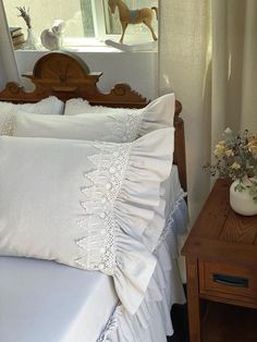 a bed with white sheets and pillows on top of it next to a wooden night stand