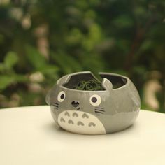 a gray and white cat planter sitting on top of a table next to green plants