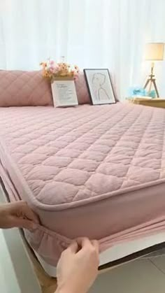 a person is placing a mattress on top of a bed with pink sheets and pillows