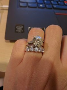 a person's hand with a ring on it and a laptop in the background