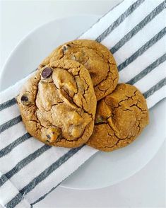 three chocolate chip cookies sitting on top of a white plate next to a black and white towel