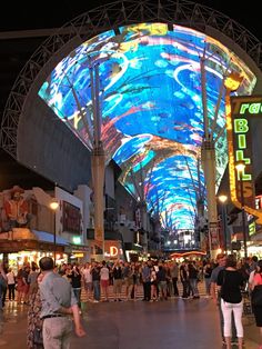 people are walking around in an indoor shopping area at night time with colorful lights on the ceiling