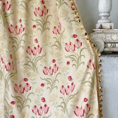 a curtain with pink flowers on it in front of a white vase and lamp stand