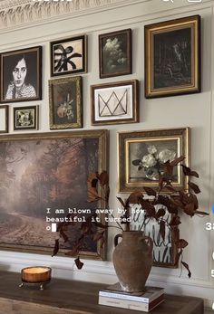 a room with many framed pictures on the wall and a vase full of flowers in front of it