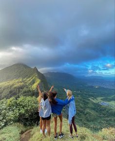 three girls standing on top of a hill with their arms in the air