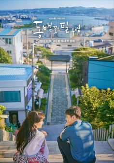 a man and woman sitting on the steps looking at each other in front of some buildings