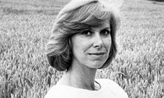 a black and white photo of a woman standing in a wheat field looking at the camera