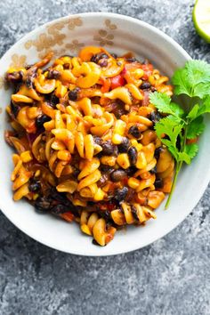 a white bowl filled with pasta and beans next to cilantro on a gray surface