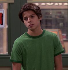 a young man in a green t - shirt is looking at the camera