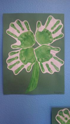 a green and white flower painted on the wall next to a blue wall with two hands