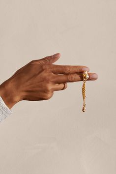 a hand holding a gold chain with a bead on it's end and a ring in the middle